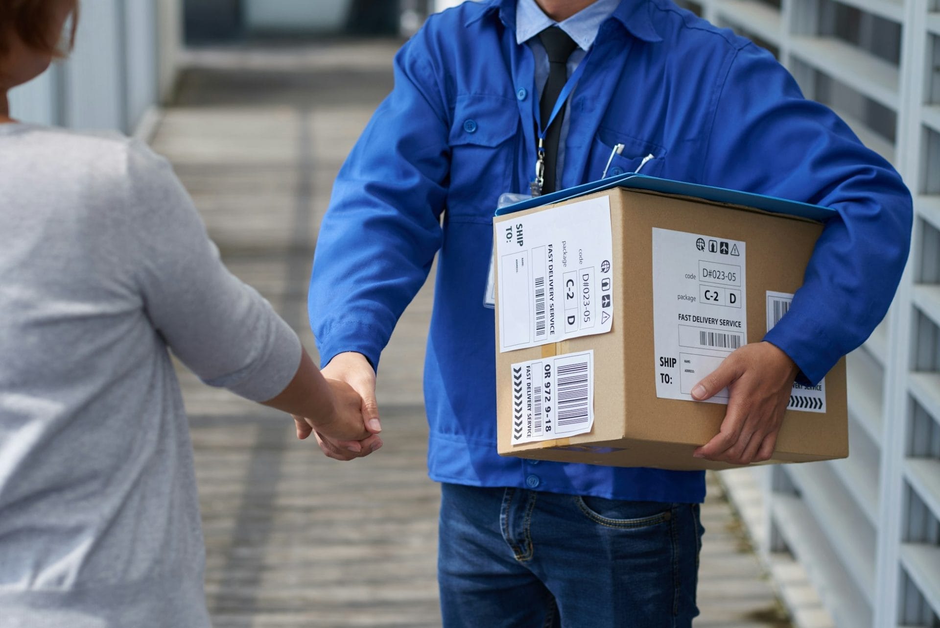 Delivery man greeting a customer by shaking hand before handing out a parcel